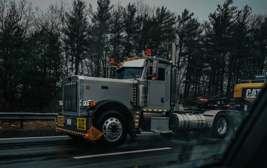 Heavy-haul tractor pulling an excavator on a lowboy trailer in the rain